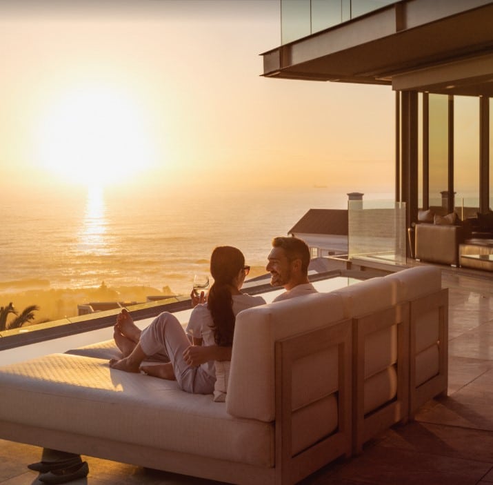 A couple watches the sunset from their luxury home balcony overlooking the ocean.